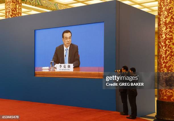 Two photographers take photos of Chinese Premier Li Keqiang as a live image of him is seen on a screen behind them during a press conference after...