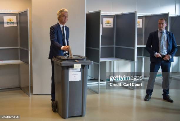 Close protection police officer looks on as Geert Wilders , the leader of the right-wing Party for Freedom , casts his vote during the Dutch general...