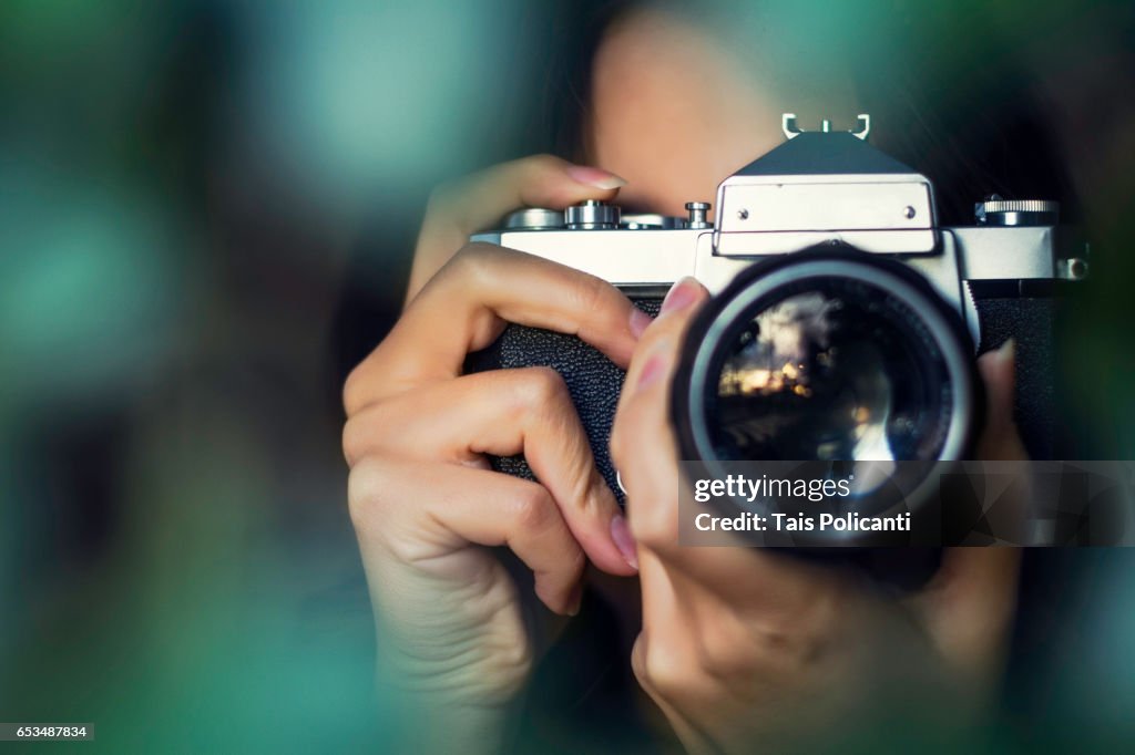 Woman photographer shooting with an analog camera between tree leaves at sunset - Hessen, Germany