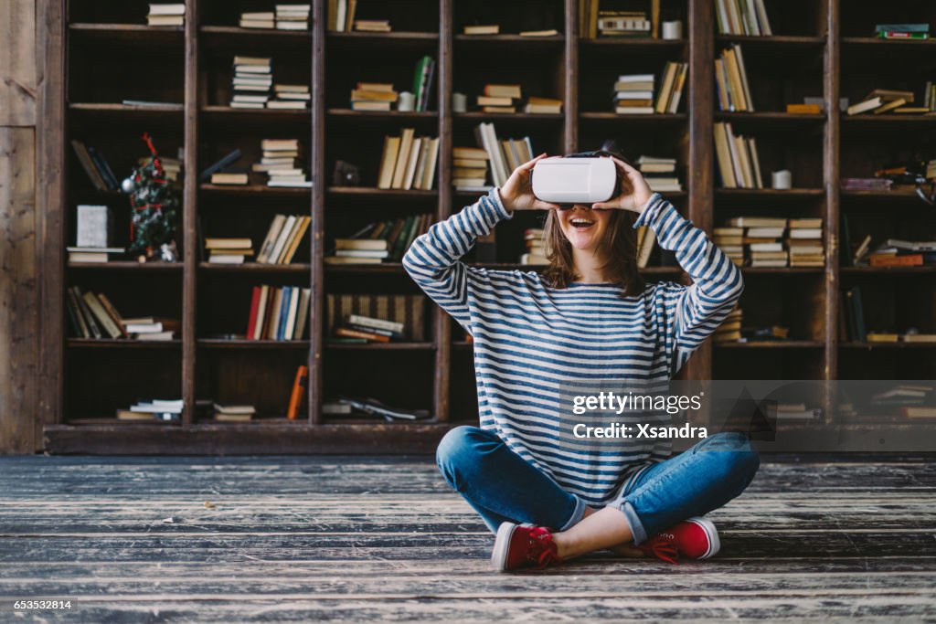 Glückliche Frau mit VR-Brille vor Bücherregalen