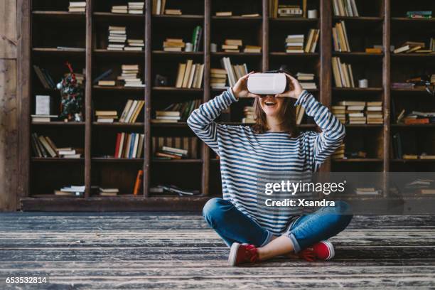 happy woman wearing vr glasses in front of bookshelves - augmented reality stock pictures, royalty-free photos & images