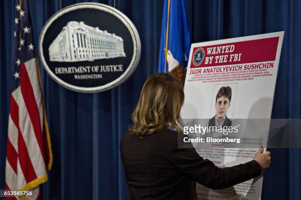 An employee places a wanted poster for Igor Anatolyevich Sushchin on display before a news conference at the Department of Justice in Washington,...