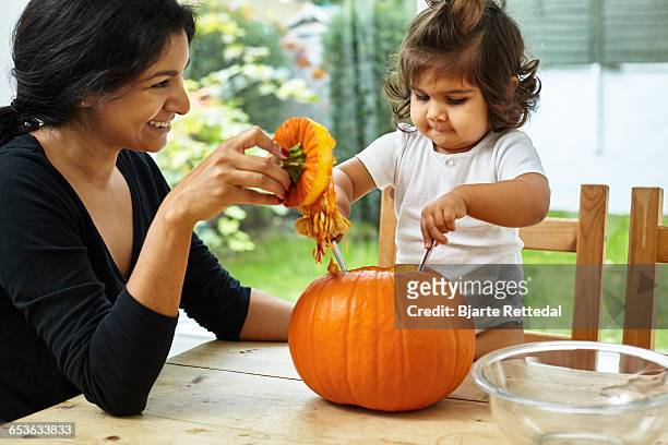 mother and baby daughter carving a pumpkin - bjarte rettedal stock pictures, royalty-free photos & images