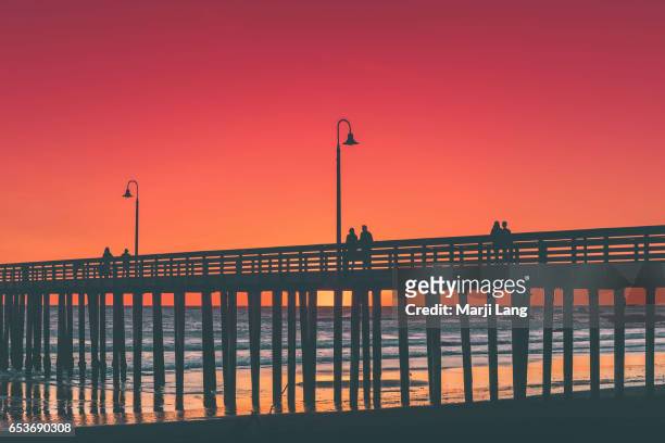 Couples watching sunset by the Pacific ocean from the Pier in Cayucos, California, USA.