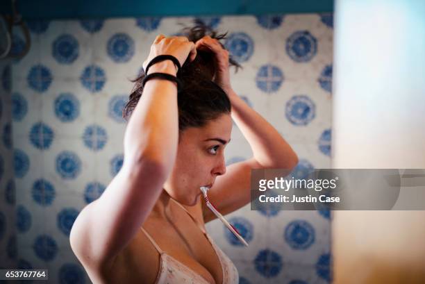 woman fixing her hair and brushing teeth at the same time - preparazione foto e immagini stock
