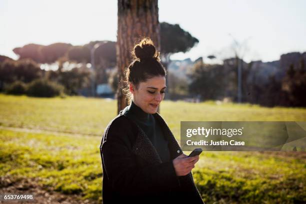 woman using her simple mobile phone in the park - topknot stock-fotos und bilder