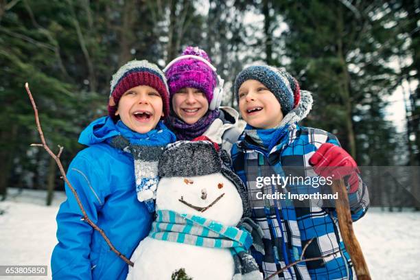 three kids building a snowman on winter day - making a snowman stock pictures, royalty-free photos & images