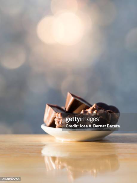 small plate of porcelain with chocolates of chocolate on a table of wood, illuminated by the natural light of the sun - vollmilchschokolade stock-fotos und bilder