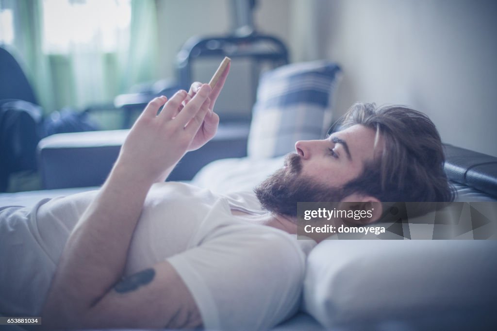 Handsome bearded man using phone in the bed