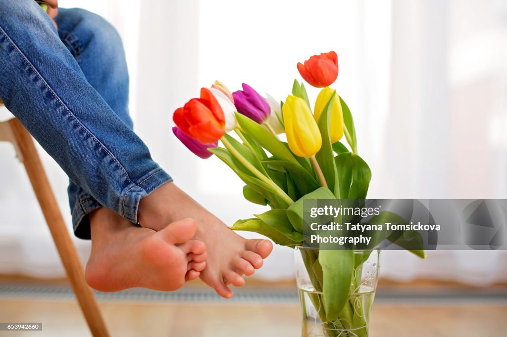 Little kid fee, child sitting on a chair at home, vase with tulips next to them, back light