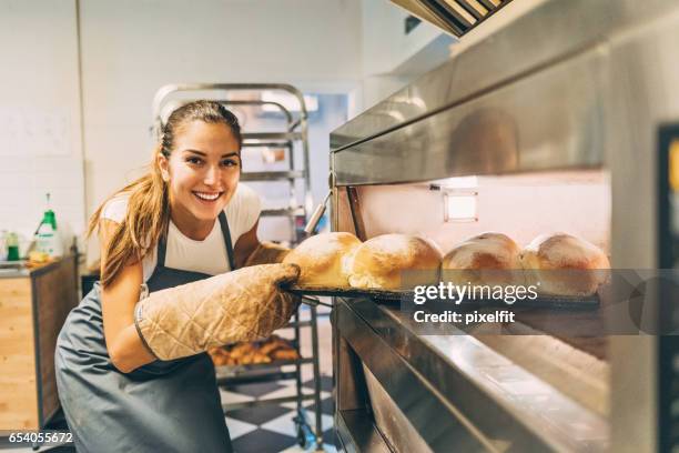 beautiful baker removing the hot bread from the oven - baker smelling bread stock pictures, royalty-free photos & images