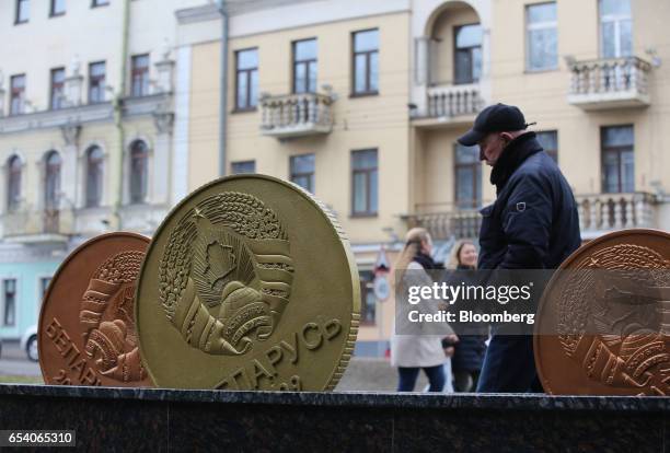 Pedestrians pass a street sculpture representing Belarussian ruble currency coins near the finance ministry in Minsk, Belarus, on Wednesday, March...