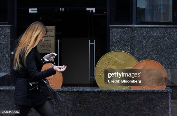 Pedestrian passes a street sculpture representing Belarussian ruble currency coins near the finance ministry in Minsk, Belarus, on Wednesday, March...