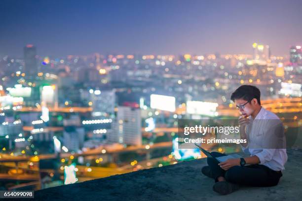 jonge zakenman met laptop en digitale tablet stadsgezicht achtergrond - trading resumes at the stock exchange of thailand stockfoto's en -beelden