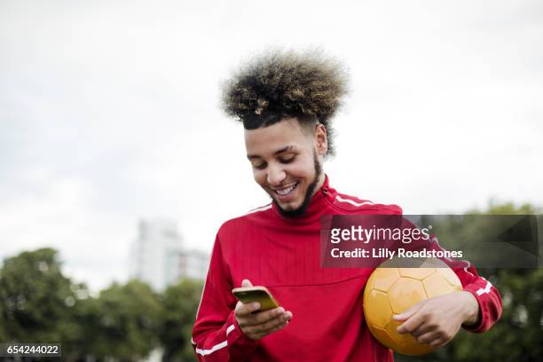 young guy texting while holding ball - football phone foto e immagini stock