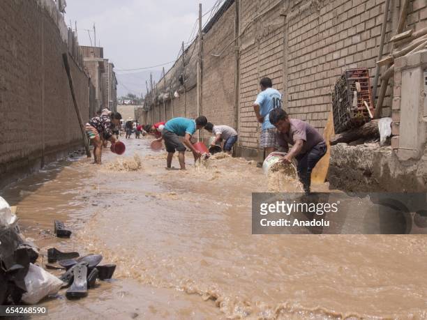 People use buckets to remove the mud and water left by a flood after Huaycoloro river overflowed in the area of Carapongo, a few kilometers from...