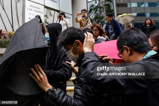 Supporters use umbrellas to cover their faces while surrounded by members of the media, as they leave the District Court in Hong Kong on March 17...