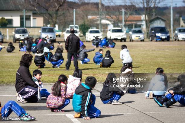 Students at the Hokuyou Elementary School are seen sitting on the ground during a missile evacuation drill on Friday, March 17 in Kitaura, Oga, Akita...