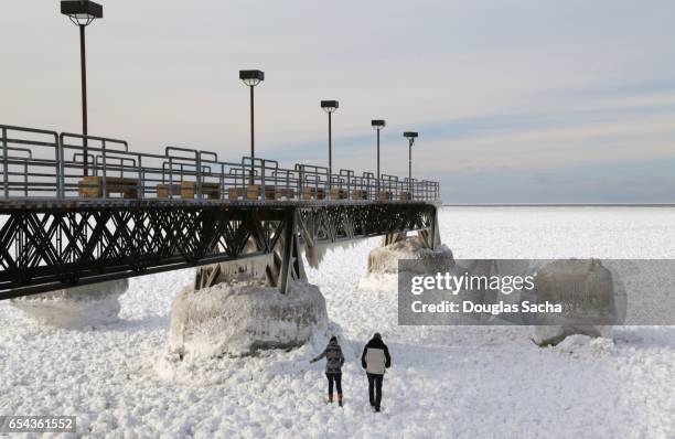 couple walks on the frozen lake passing a fishing pier above - ice storm stock pictures, royalty-free photos & images