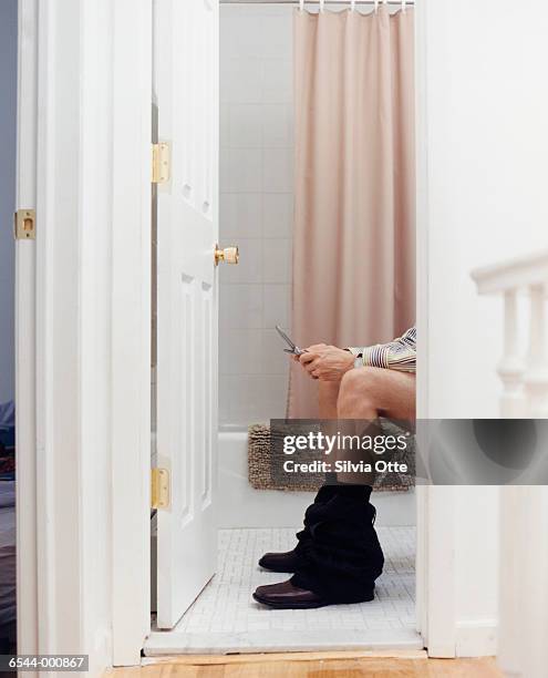 man on toilet using cell phone - bathroom door imagens e fotografias de stock
