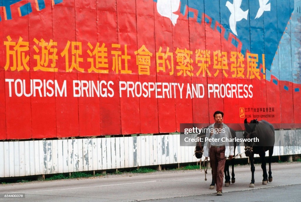 A man leads two ponies past a huge advertising billboard...