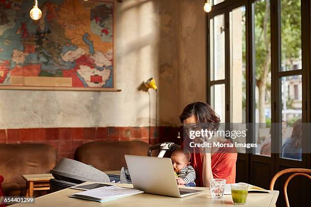 mother carrying baby using technologies at table - working mom stock pictures, royalty-free photos & images