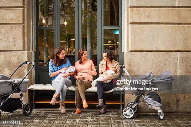 expectant and friends with babies sitting on bench - kinderwagen stockfoto's en -beelden