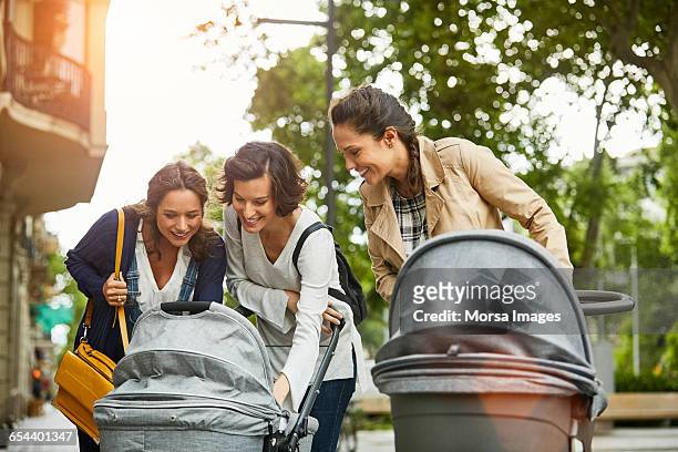 female friends looking into baby stroller at park - femme poussette rue photos et images de collection