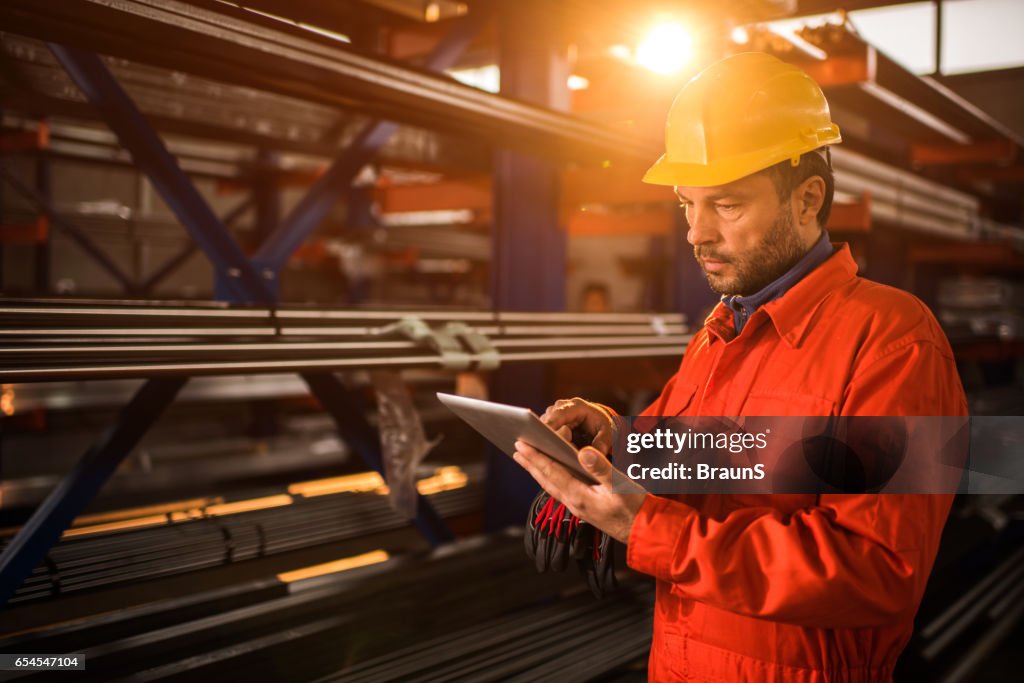 Trabajador manual con tableta digital en edificio industrial.