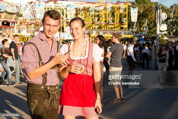 young couple playing with smartphone at the oktoberfest - oktoberfest home stock pictures, royalty-free photos & images