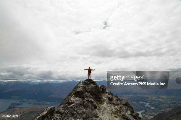 male hiker stands on mountain summit, arms outstretched - standing on mountain peak stock pictures, royalty-free photos & images