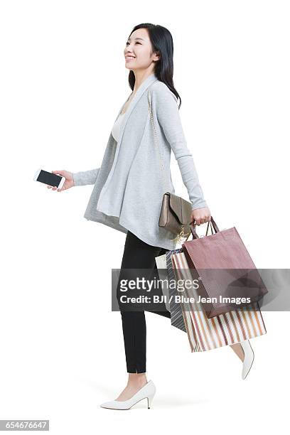 happy young woman holding a smart phone and shopping bags - shopping bags white background stock pictures, royalty-free photos & images