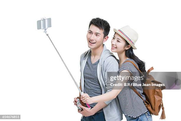 young couple taking self portrait with a smart phone - selfie stick white background stock-fotos und bilder