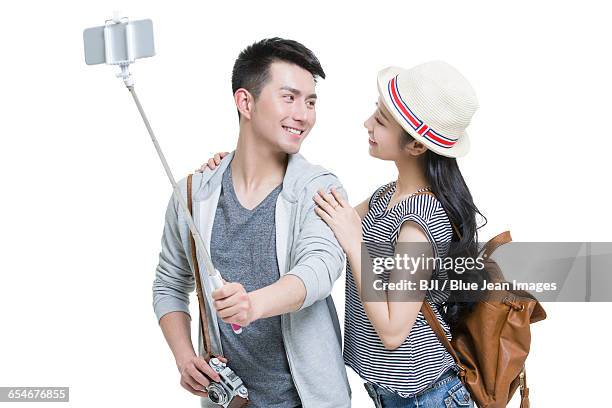 young couple taking self portrait with a smart phone - selfie stick white background stock-fotos und bilder