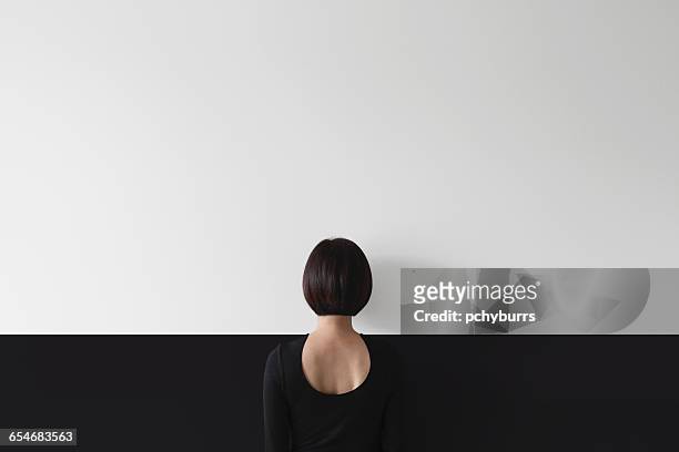 rear view of woman standing facing wall - tarnung stock-fotos und bilder