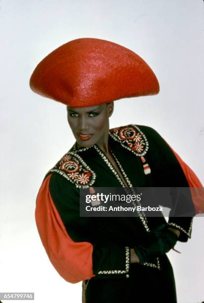 Portrait of Jamaican-born model, singer, and actress Grace Jones as she poses in a bright red hat and multi-colored top, New York, New York, late...