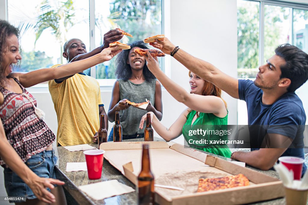 Cheerful friends enjoying pizza and beer at home