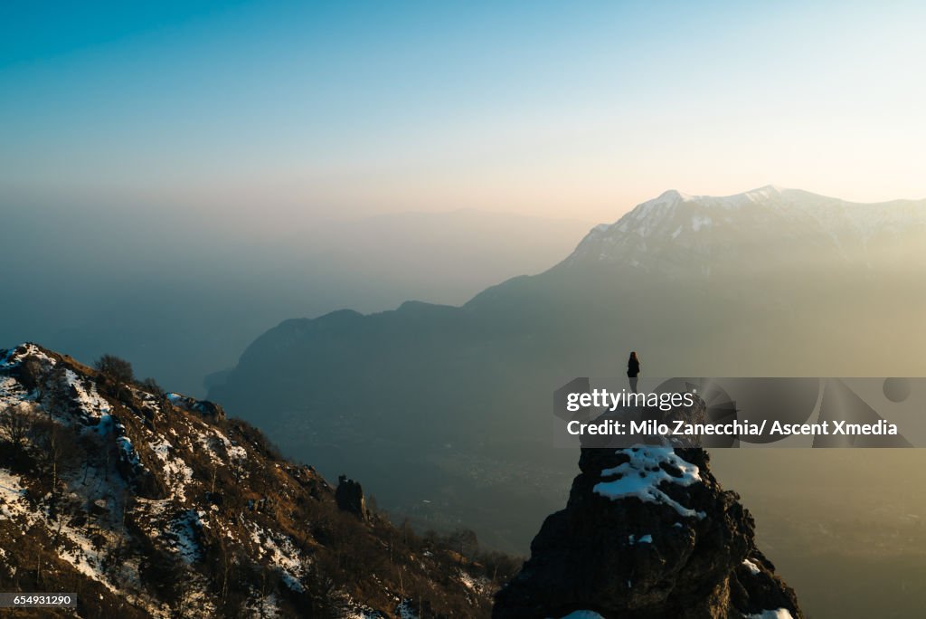Female hiker stands on mountain summit, looks off