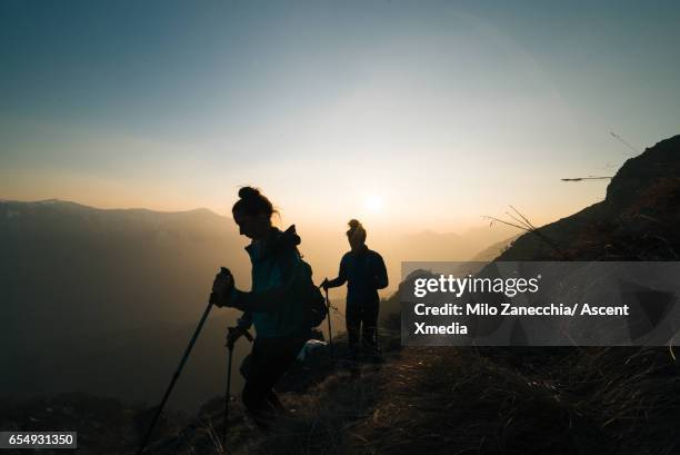 two female hikers follow trail from mountain summit - kanton tessin stock-fotos und bilder