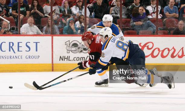 Lawson Crouse of the Arizona Coyotes and Zach Sanford of the St Louis Blues battle for a loose puck in front of Magnus Paajarvi of the Blues during...