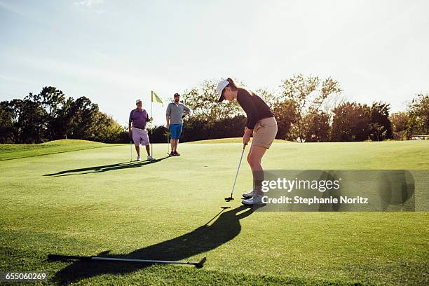 woman putting on golf course with family watching - golf fotografías e imágenes de stock