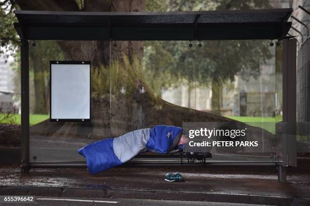 This photo taken on March 17, 2017 shows a man sleeping in a bus shelter near Sydney harbour in Sydney. Homelessness is on the rise in Australia,...