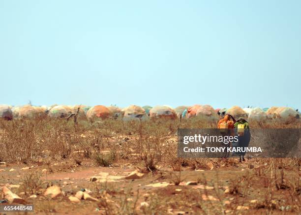 Women carrying jerrycans of water from a collection point set up by a UN aid agency walk on March 14, 2017 towards a makeshift camp on the outskirts...