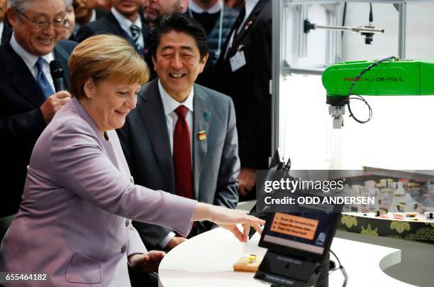 German Chancellor Angala Merkel and Japanese Prime Minister Shinzo Abe visit a booth with a robotic arm picking up sushis as they tour the CeBIT...