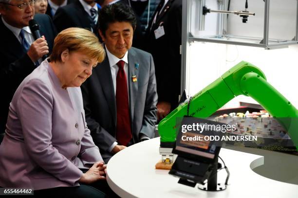 German Chancellor Angela Merkel and Japanese Prime Minister Shinzo Abe visit a booth with a robotic arm picking up sushis as they tour the CeBIT...