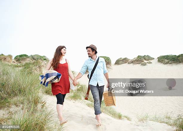 couple walking to beach with picnic basket. - picnic basket stock pictures, royalty-free photos & images