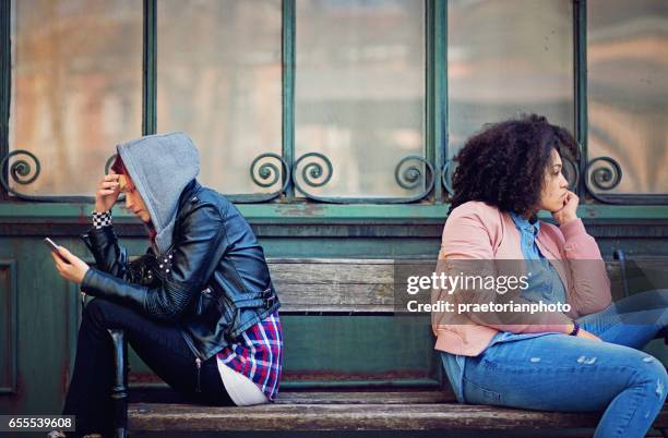 girlfriends in conflict are sitting on the bench and sulking each other - friends loneliness imagens e fotografias de stock