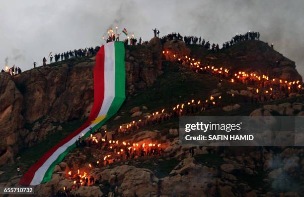 Iraqi Kurds holding lit torches walk up a mountain, draped in a large Kurdish flag, in the town of Akra, 500 km north of Baghdad, on March 20, 2017...