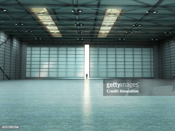 man in an empty warehouse with door open - hanger foto e immagini stock