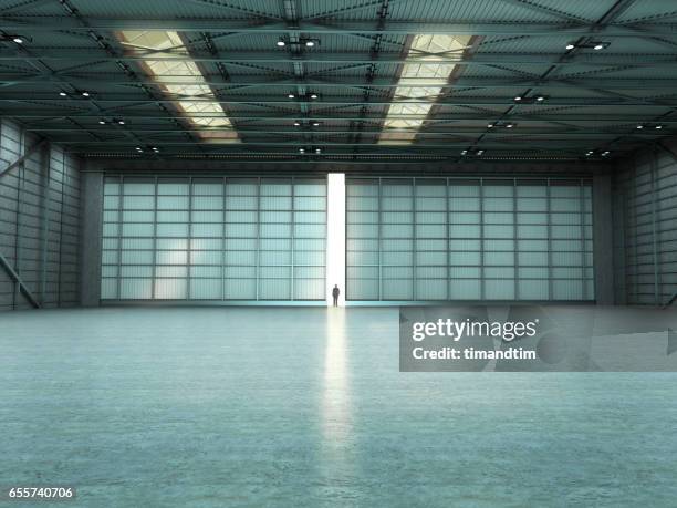 man in an empty warehouse with door open - hangar stockfoto's en -beelden